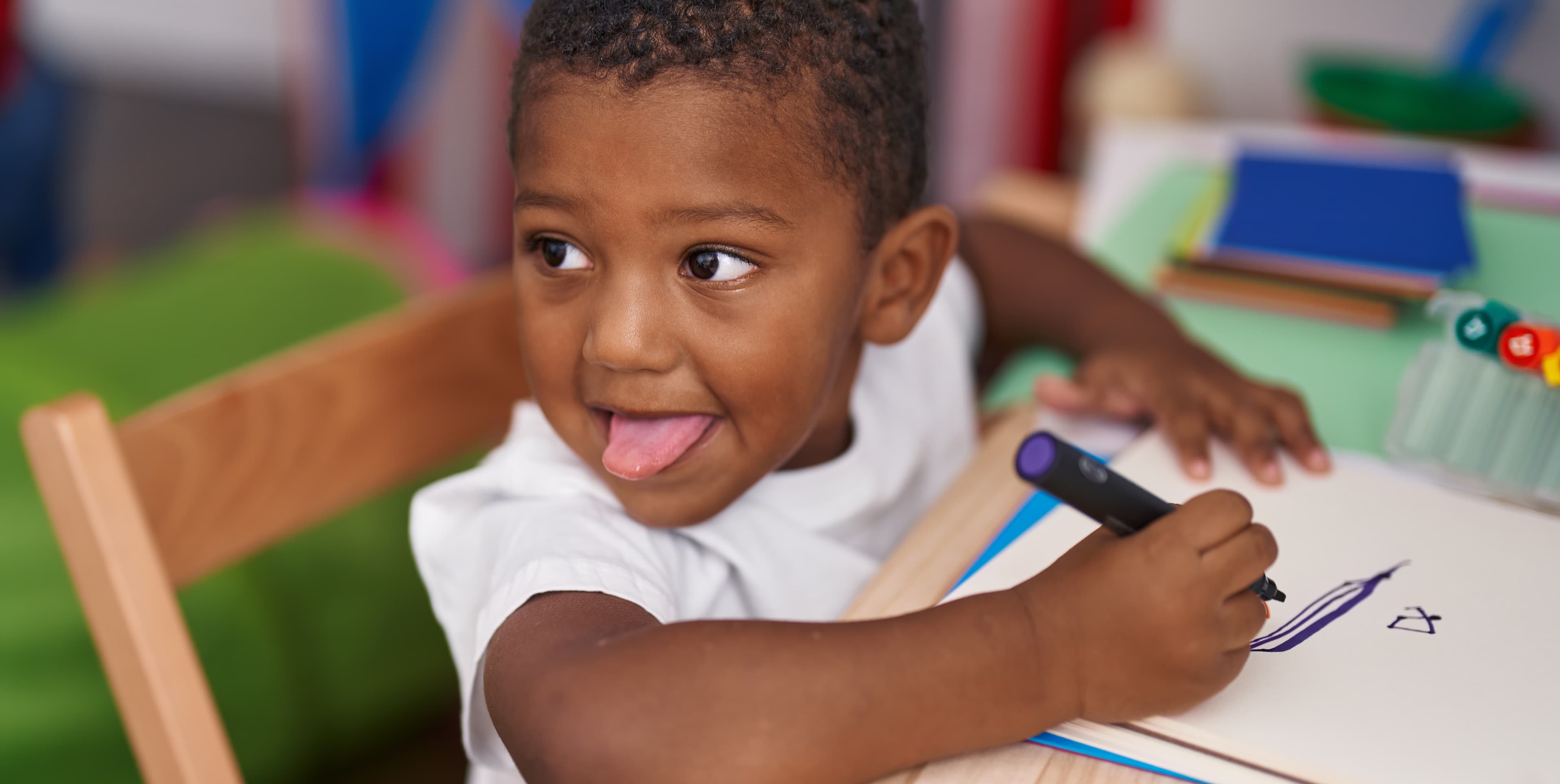 Élève de maternelle dessinant dans son cahier, assis à sa table
